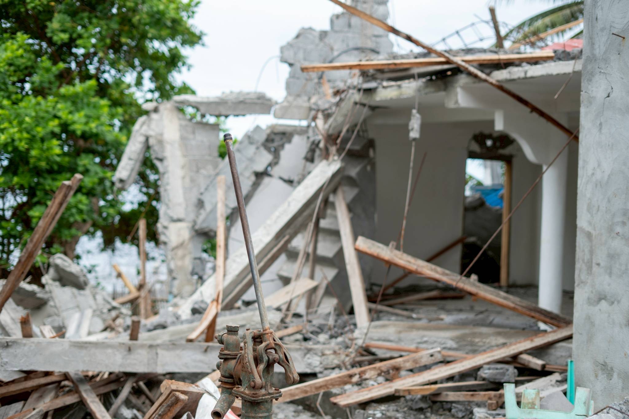 A deep well water pump in the foreground is all that remains of a house that crumbled from the violent shaking of the June 8 quake.