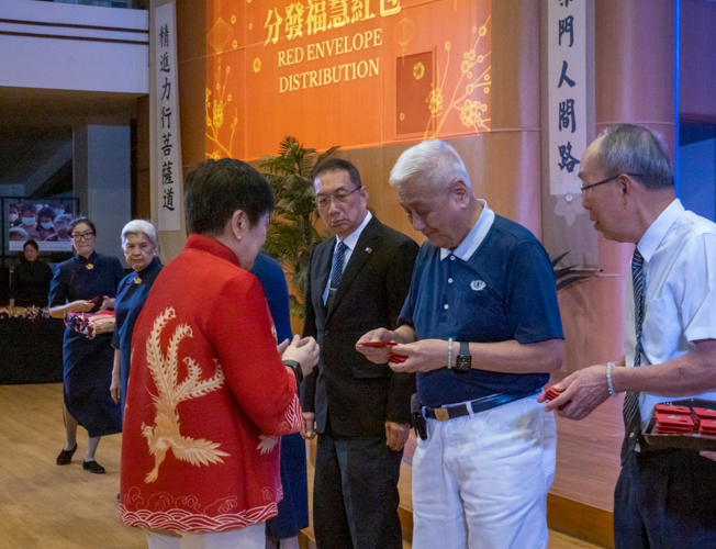 Tzu Chi Philippines CEO Henry Yuñez (second from right) leads in the distribution of angpao, red envelopes containing commemorative coins from Master Cheng Yen. Here, he presents Mrs. Betty Ang with an envelope as her husband, Ambassador Francis Chua (in suit), looks on.