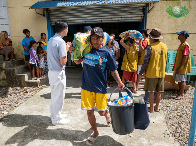 A resident steps out of the distribution center, loaded with a sack of rice and groceries.
