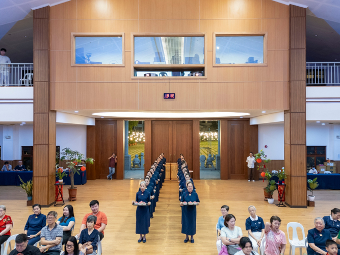 Volunteers carrying trays of lotus candles for guests slowly make their way to the front of the Jing Si Auditorium.