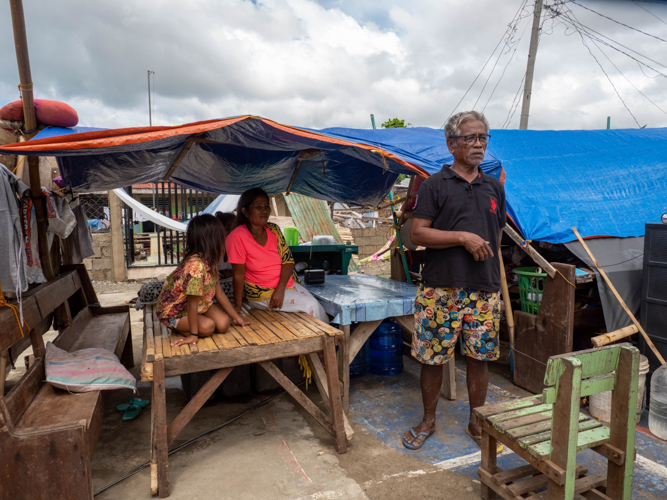 Barangay Lawis fisherman Miropo Husalam (standing) creates a makeshift home for his family using tarpaulin, tables, and a church pew. 【Photo by Marella Saldonido】