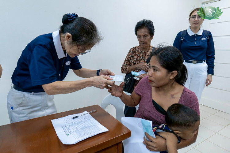 Tzu Chi volunteer Elvira Chua (left) bows as she hands financial assistance to a resident whose house was destroyed, while Tzu Chi volunteer Mary Ann Lu (far right) looks on.