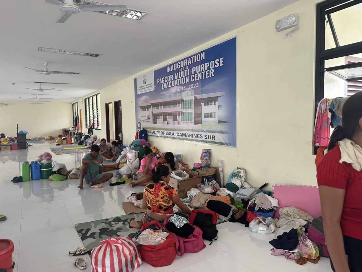 At the PagCor Multi-purpose Evacuation Center, families settle on the floor with the items they were able to salvage from their houses during evacuation.