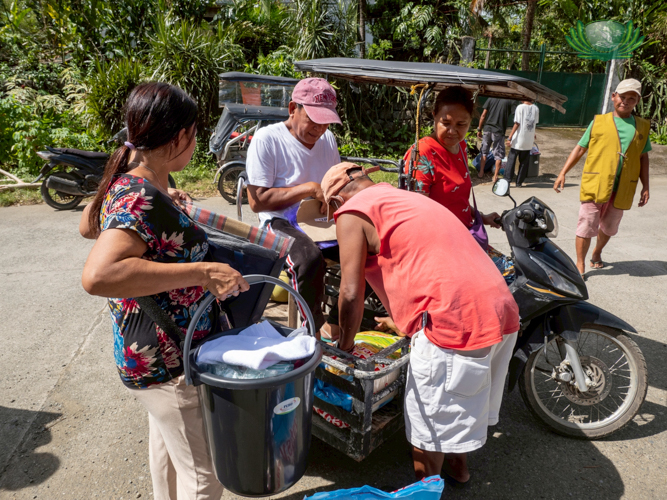 Residents assist each other in loading groceries onto a motorcycle, smiles evident on their faces as they go home.