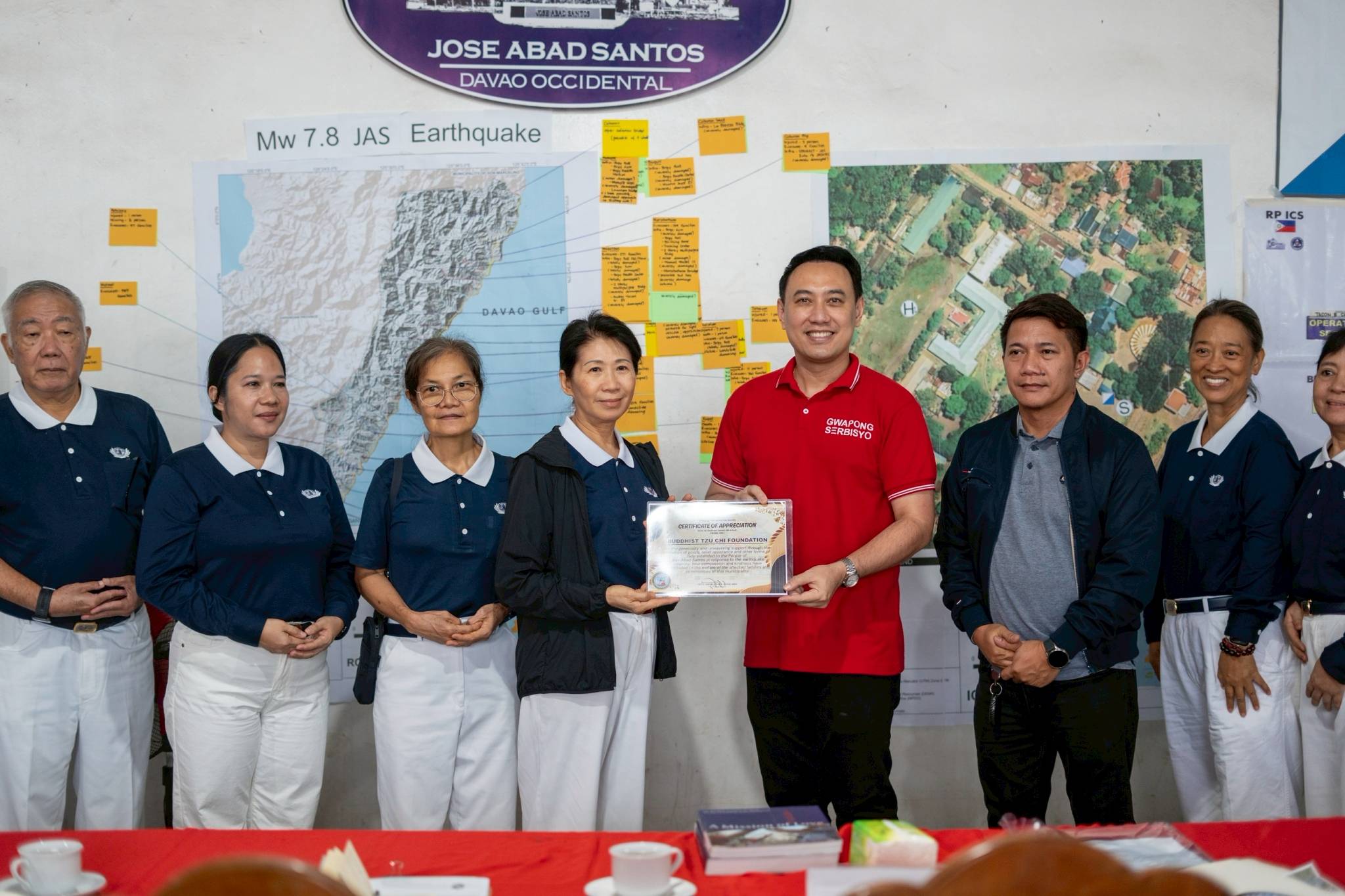 Jose Abad Santos Mayor Jason John A. Joyce (in red) presents Tzu Chi volunteers with a certificate of appreciation for traveling from Manila and Davao “to the to the farthest end of the Philippines to see our reality here.” Volunteers arrived with bread and emergency medicines and the promise to return with more aid for evacuees. 
