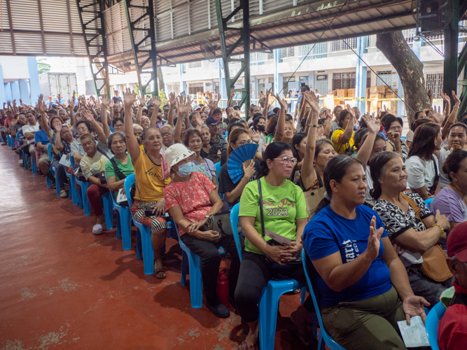 Beneficiaries raise their hands as stamp numbers of their relief stubs are announced.