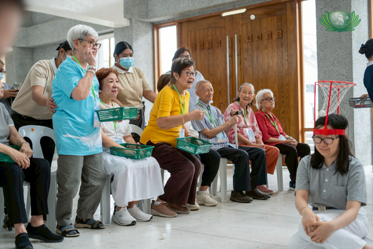 Seniors take turns shooting ping pong balls into a basket attached to a volunteer’s head.