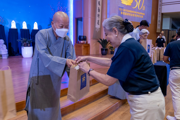 Dharma Master De Pei (left) hands out the anniversary souvenir to a Tzu Chi volunteer.