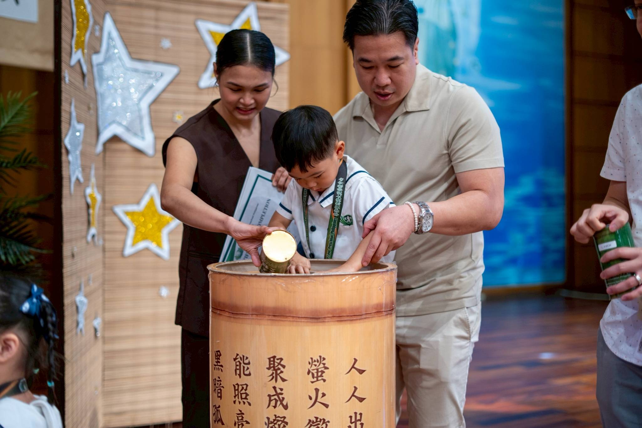 After receiving their certificate, preschoolers drop their coin bank donations in a large bamboo bank.