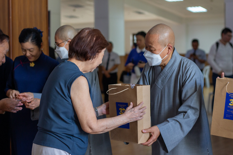 Dharma Master De Pei (left) hands out the anniversary souvenir to a guest.