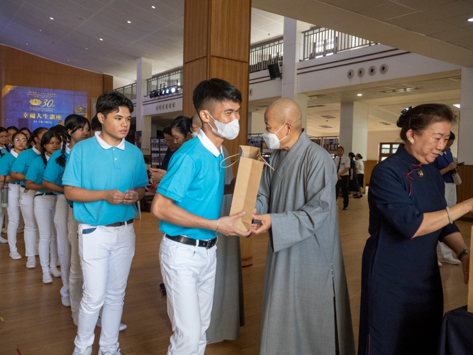 Dharma Master De Pei hands out the anniversary souvenir to Tzu Chi scholars.