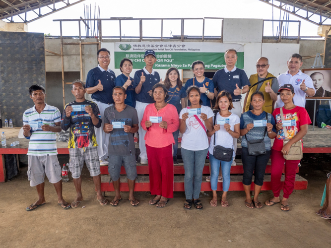 Tzu Chi volunteers pose for a photo with beneficiaries whose homes were totally damaged after the typhoon. They each received a voucher for construction materials. 