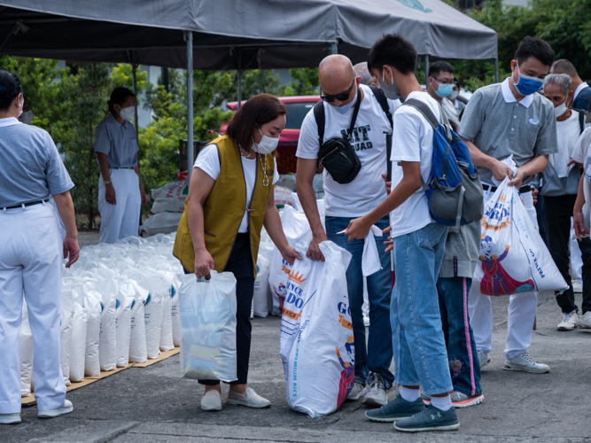 Volunteer Gretchen Velarde assists beneficiary Carlito Alba (in sunglasses) and his children with their rice and grocery relief. 【Photo by Daniel Lazar】