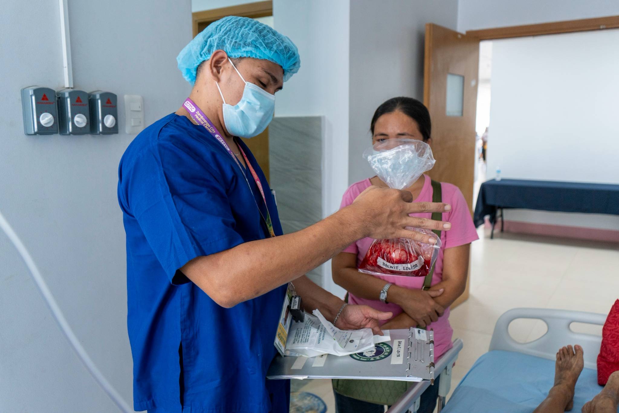 A healthcare worker shows a patient’s companion the goiter that was removed from the patient’s neck.