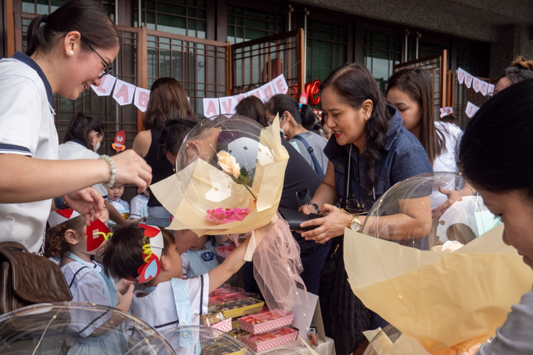 A student sells beautifully decorated balloons with roses to enthusiastic parents.