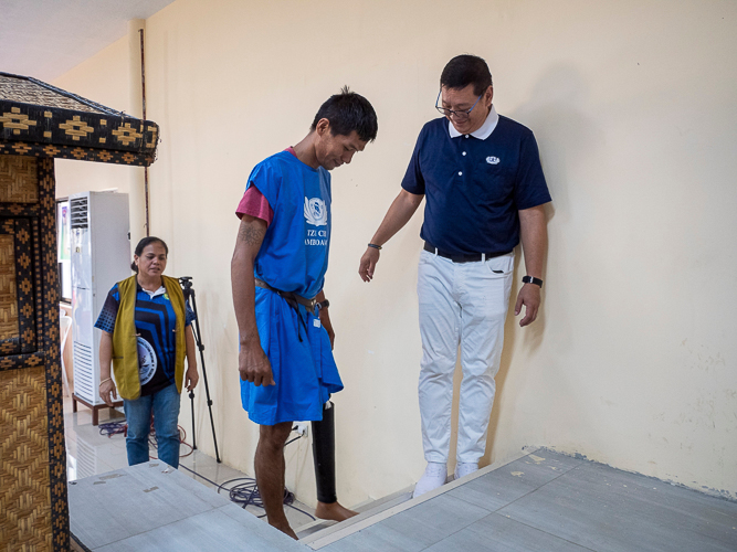 Tzu Chi Zamboanga Liaison Officer Dr. Anton Mari Lim (right) guides prosthesis recipient Joey Bolandrina (center) as he tests out his new prosthetic leg.