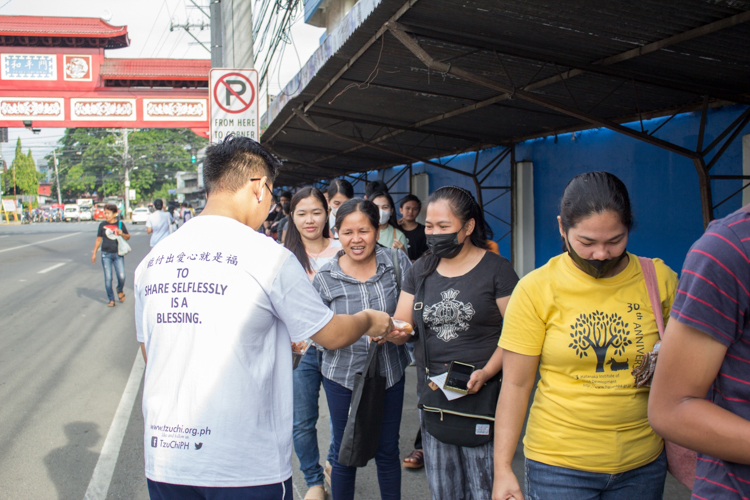 A Tzu Chi volunteer distributes snacks to beneficiaries waiting outside Davao Chong Hua High School. 【Photo by Marella Saldonido】