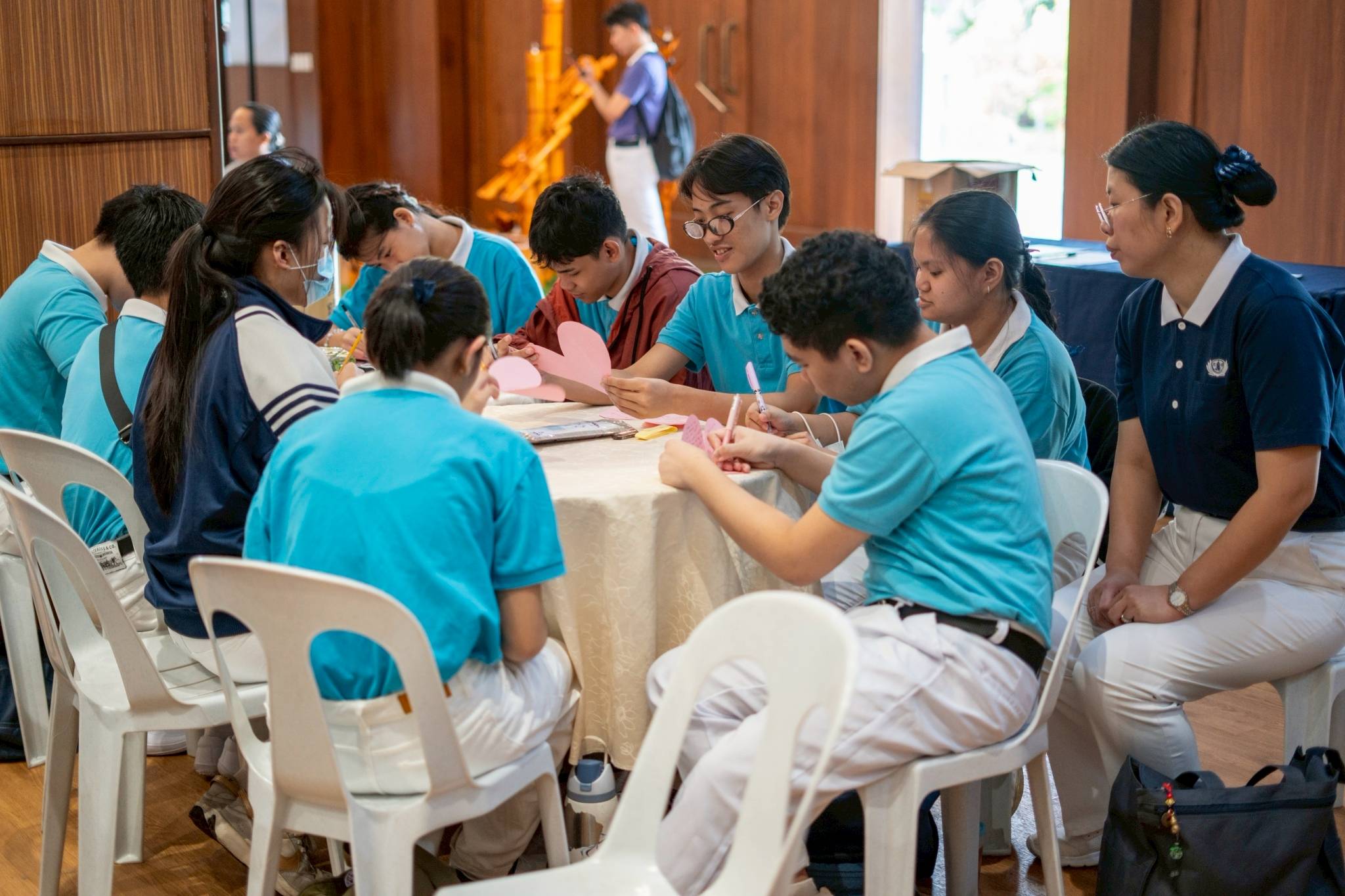 In the activity “From Hearts to Hearts,” scholars wrote their name on a paper heart and passed it on to their seatmate, who wrote a message to that scholar before passing it to their seatmate. The paper hearts were continuously passed and written on until they reached their original owner.