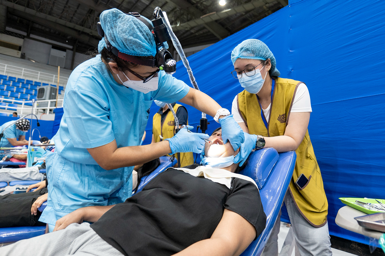 A volunteer steadies a patient’s head as a dentist administers lidocaine. 