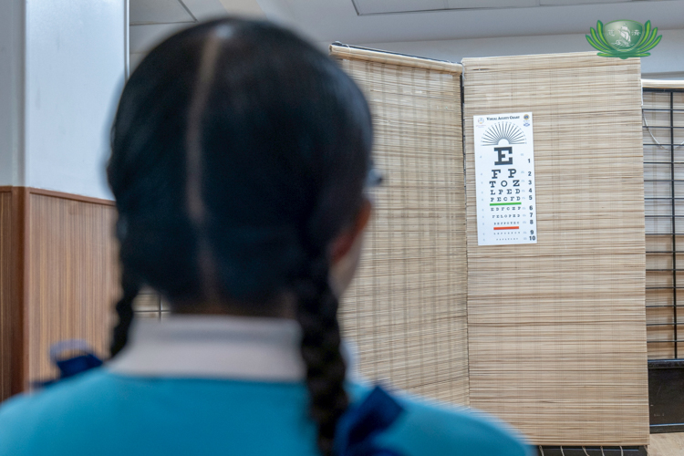 A scholar reads letters on a Snellen chart during a visual acuity test conducted by an optometrist.