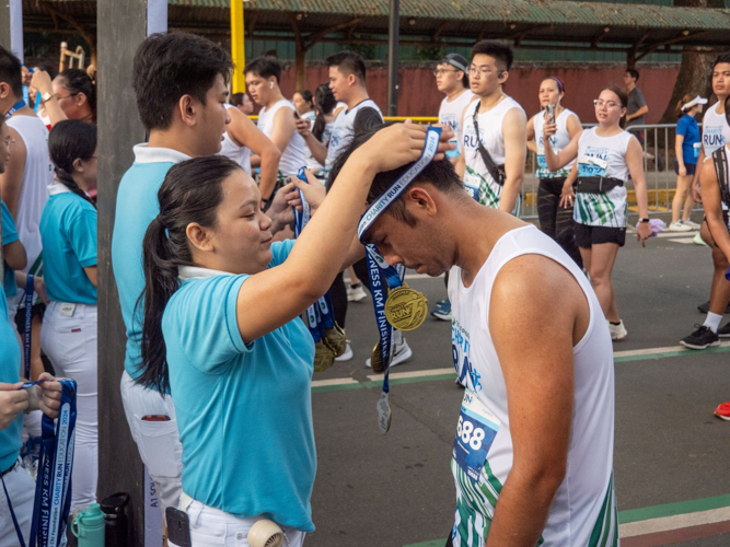 A scholar awards a runner with a finisher’s medal.