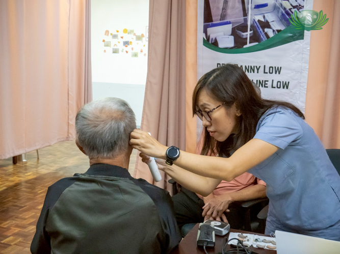 Clinical audiologist Kristine Layson (right) uses an otoscope to examine a beneficiary’s inner ear. 