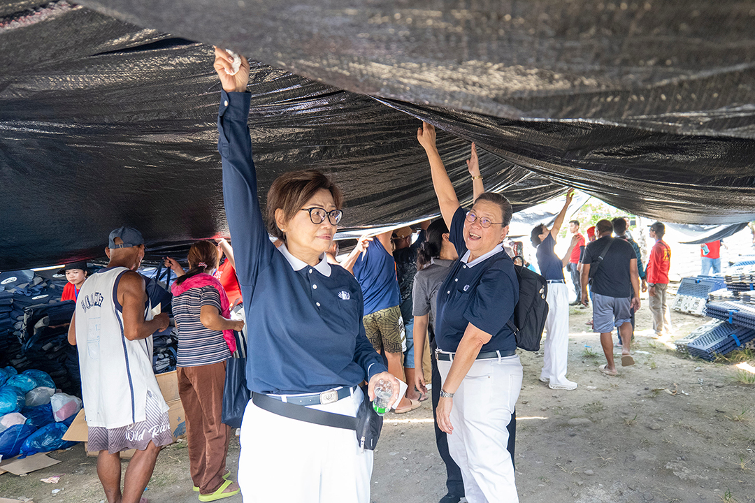 Tzu Chi volunteers Molita Chua and Judy Lao hold up the tarpaulin that served as the roofing for the distribution of relief items. 