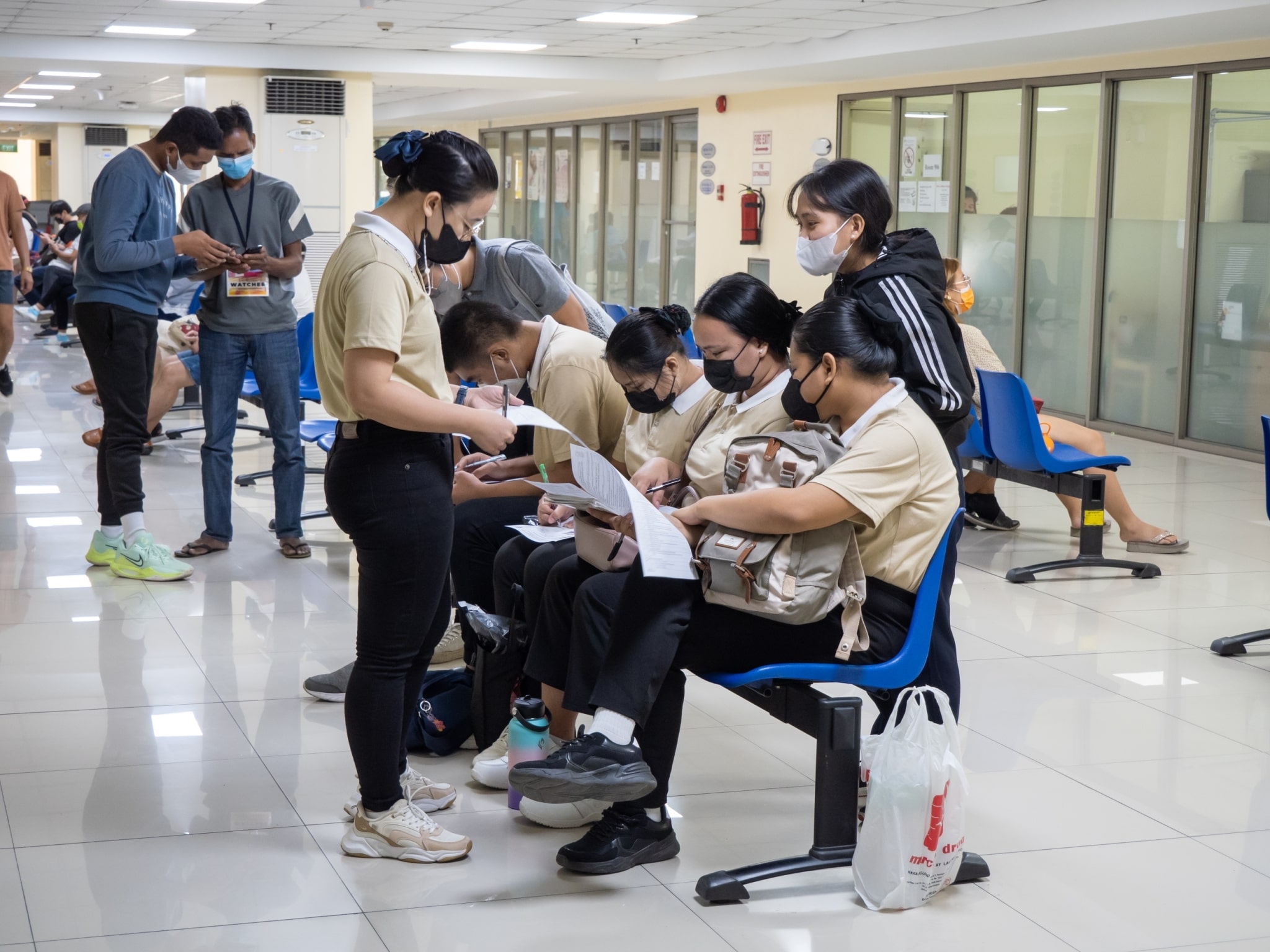 Tzu Chi caregiver scholars (in cream shirts) who volunteered to donate blood fill up forms at the Chinese General Hospital and Medical Center. In the background, Tzu Chi photographer Matt Adrian Serrano (in blue and black) confers with Andy Awel, logistics staffer at Tzu Chi’s Agno branch, whose wife is in need of blood.【Photo by Marella Saldonido】