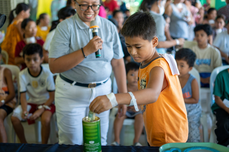 A child at the Palo Medical Mission donates to Tzu Chi’s coin bank as Tzu Chi Charity Department Head Tina Pasion looks on.