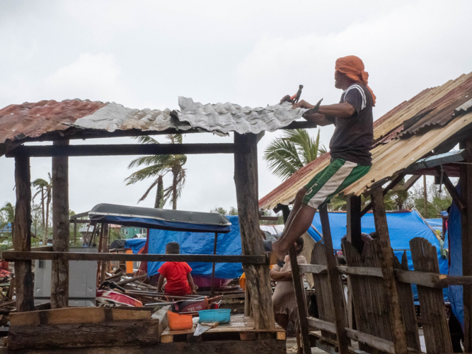 A man pieces salvaged corrugated iron sheets together to make a roof.  【Photo by Marella Saldonido】