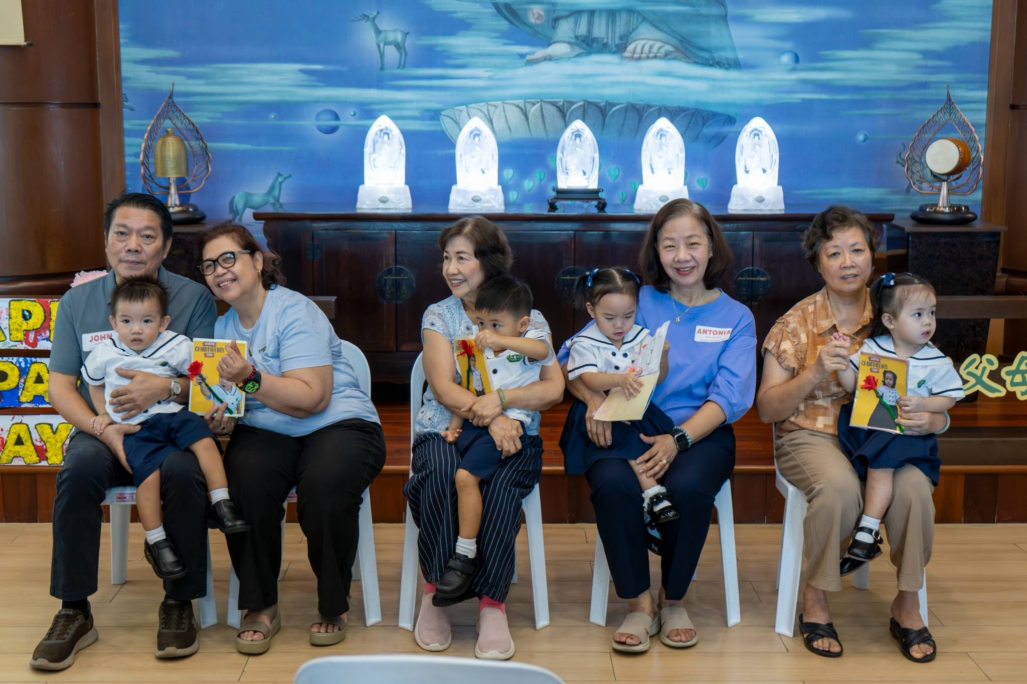 In a heartwarming moment, on stage, the young toddlers happily hand over handmade cards to their beloved grandparents.