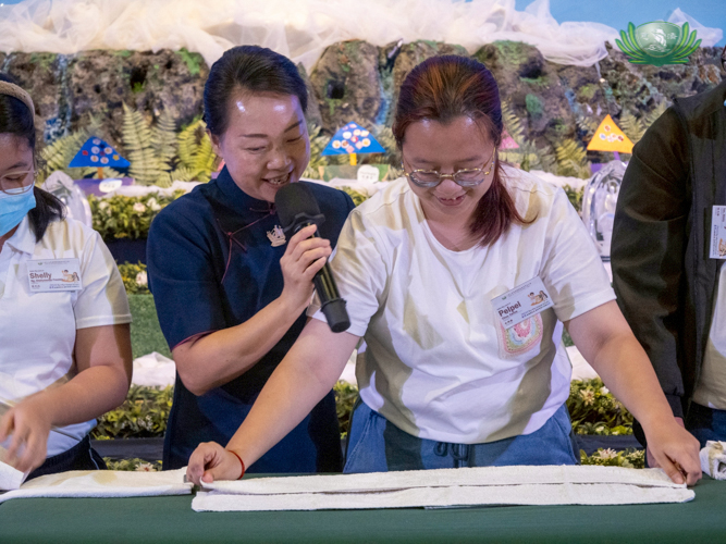 Guided by a volunteer, Carina Chua tries her hand at folding linen the Tzu Chi way.