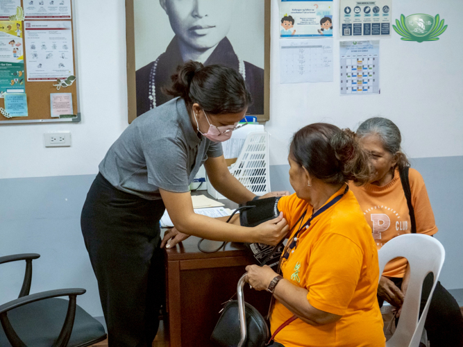 Tzu Chi volunteer Jeyziel Mae Burce (standing) checks the vital signs of patients before they are fitted with a hearing aid. 