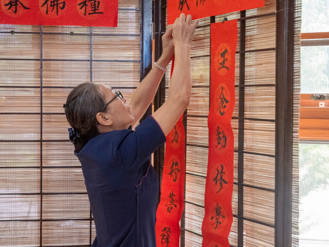 A volunteer hangs the red scrolls with Chinese characters created by Chua Hu Hua and other calligraphers during Tzu Chi’s Year End Blessing Ceremony. Typically found at the main entrance of Chinese homes during the Lunar New Year, the scrolls carry messages of goodness, peace, and joy. 