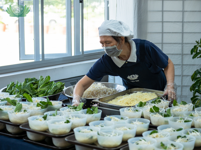 A volunteer prepares containers of vegetable noodle soup. 【Photo by Daniel Lazar】
