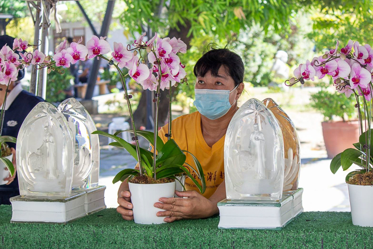 The mother of a Tzu Chi scholar carefully settles the flowers onto the table beside the crystal Buddha.