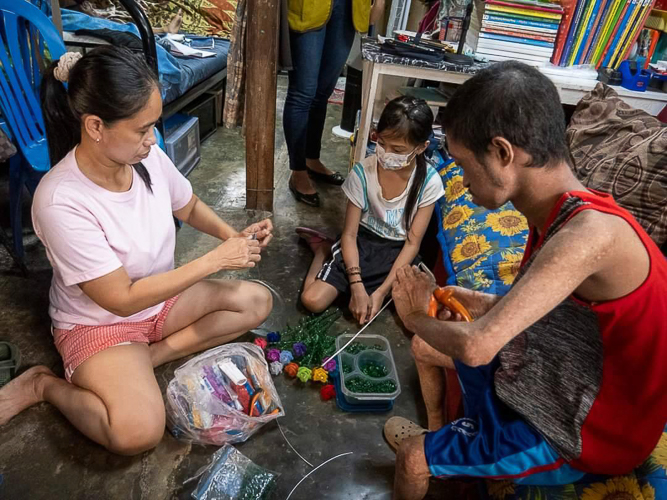 During a home visitation last September 2022, Jasper (right) and Princess (center), along with their mother Jocelyn, showed the Tzu Chi volunteers and staff how their handmade acrylic flowers are put together. 