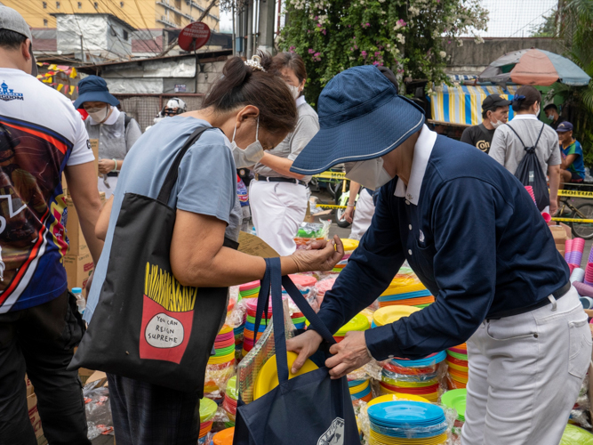 A volunteer puts a set of plates in fire beneficiary Lulu Osit’s eco bag. 【Photo by Matt Serrano】