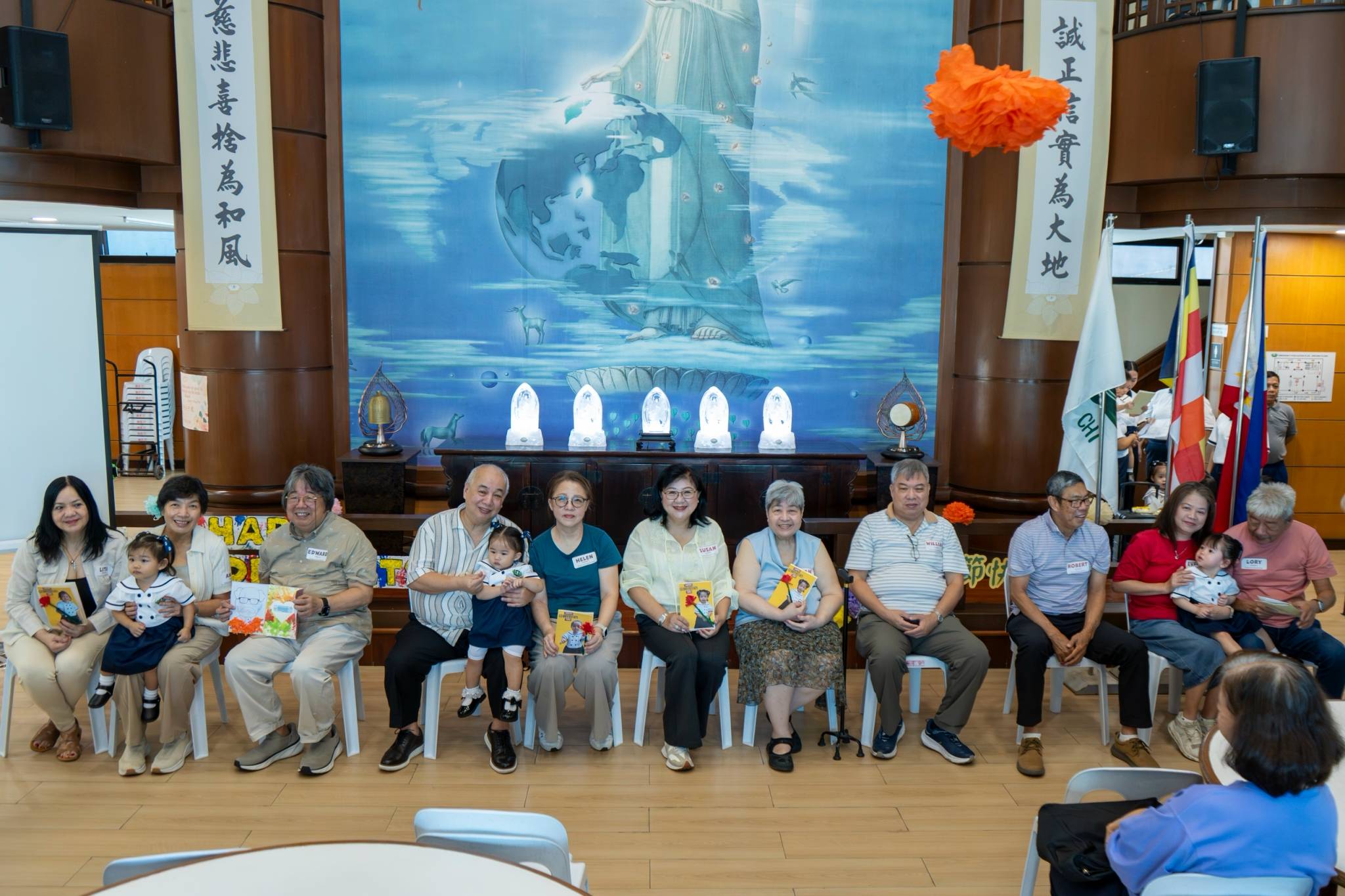In a heartwarming moment, on stage, the young toddlers happily hand over handmade cards to their beloved grandparents.