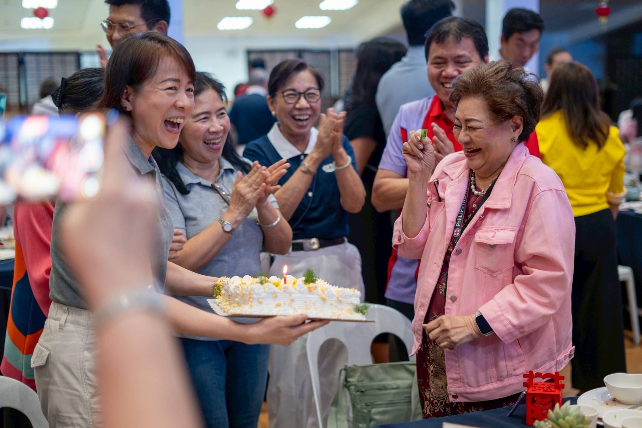 Volunteers surprise Rosalind Wee (in pink jacket) with a cake and cheers for her birthday.