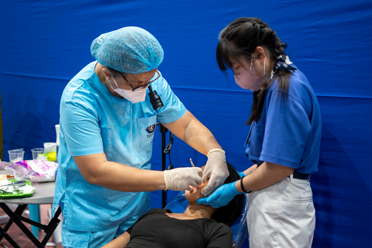 Taiwan-based Tzu Chi Youth member Sofia (Hu Zih Syuan, right) assists a dentist at work on a patient.
