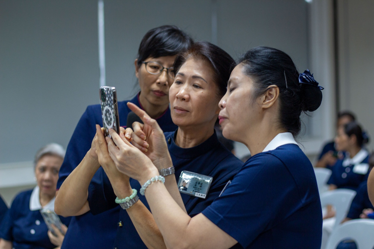 Tzu Chi Kaohsiung commissioner Yao-Ling Liao Hsin Yao (with glasses) teaches Tzu Chi volunteers Woon Ng and Pansy Ho how to use the Artificial Intelligence features in a mobile phone. 