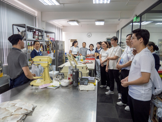 Camp participants listen to baker Bien Ang, who explains how Tzu Chi’s bakery prepares baked goods for guests and the foundation’s fundraising efforts. 