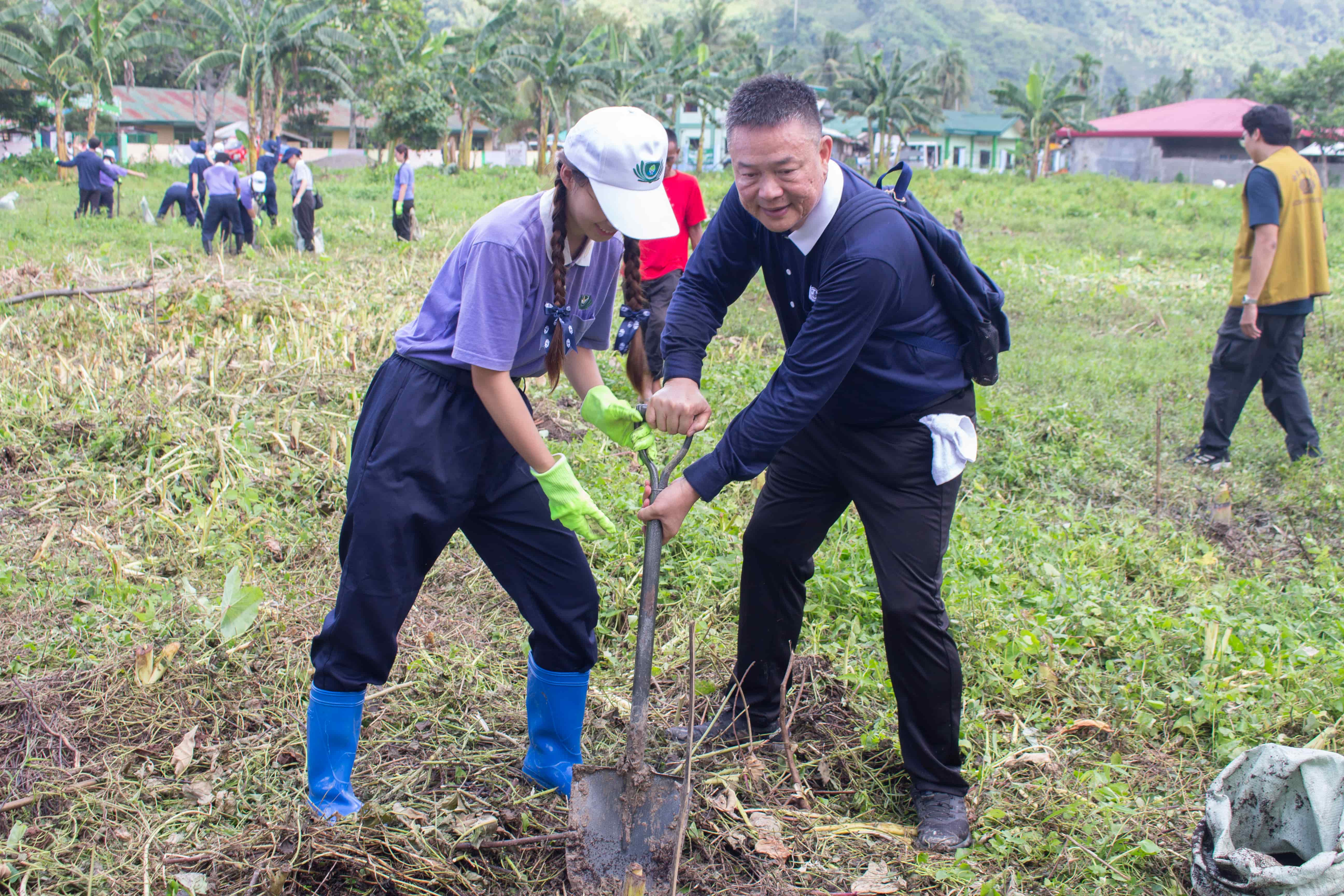 Tzu Chi Davao OIC Nelson Chua (right) guides a Tzu Chi Youth member in shoveling soil before planting the banana seedling.  