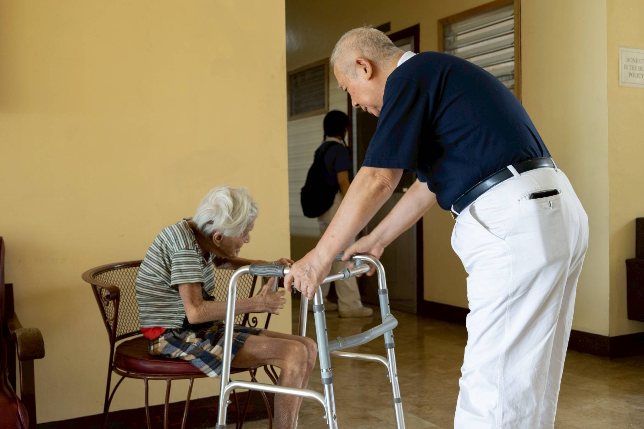 A Tzu Chi volunteer assists an elderly resident from the lobby to slowly walk toward her room at the home for the aged.
