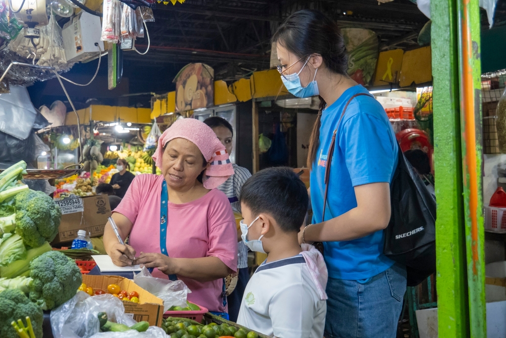 A parent (in blue) guides her son in purchasing vegetables.