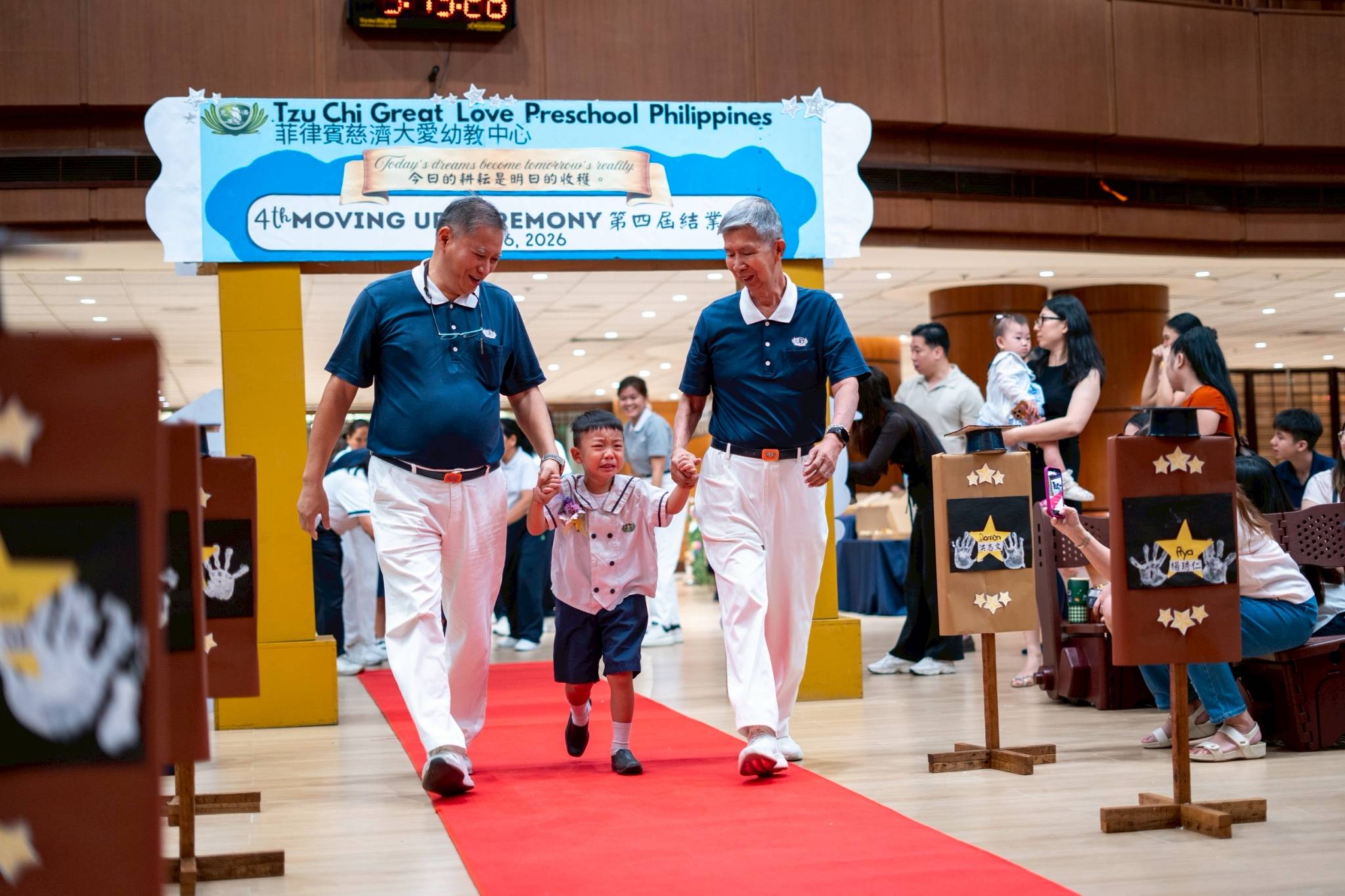 Tzu Chi volunteers Loreto Balete (left) and Rudy Ong escort an emotional nursery student on the red carpet. 
