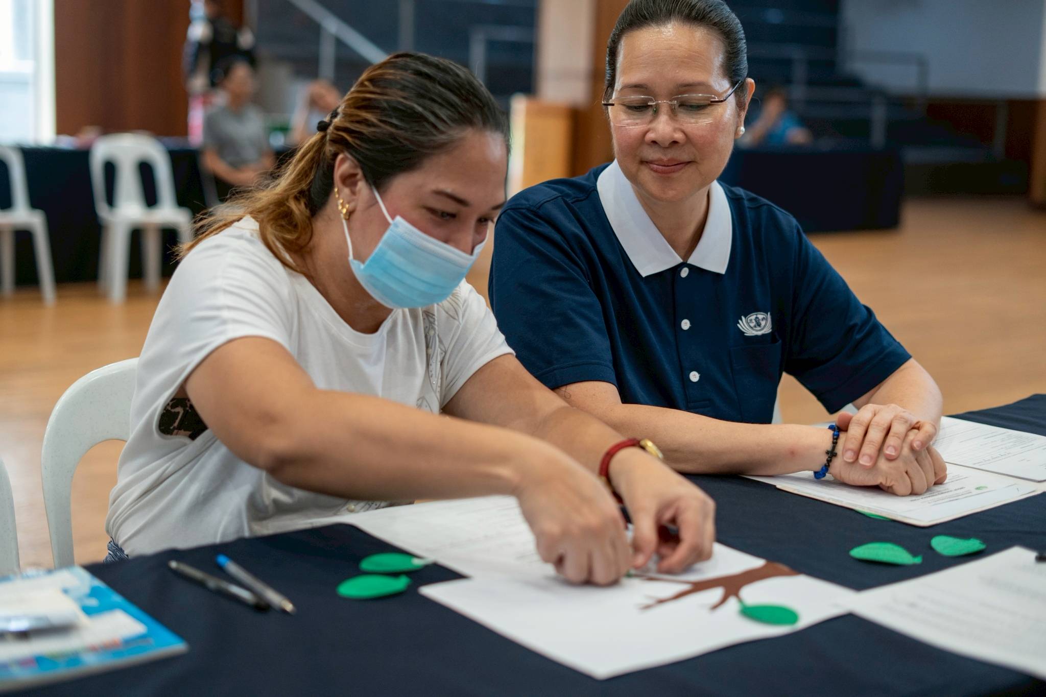 Tzu Chi volunteer Joy Gatdula watches as a medical assistance beneficiary fills her “Healthy Habit Tree” with examples on how to take better care of oneself. 