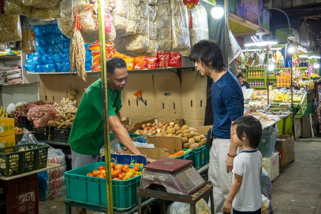 Allan Anggala (in blue), takes the lead in buying vegetables before teaching his son Ava some valuable tips to make a good purchase.