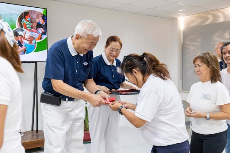 Annie Ong receives angpao from Tzu Chi Philippines CEO Henry Yuñez. The red envelope contains a commemorative coin and three rice seeds from Dharma Master Cheng Yen. 